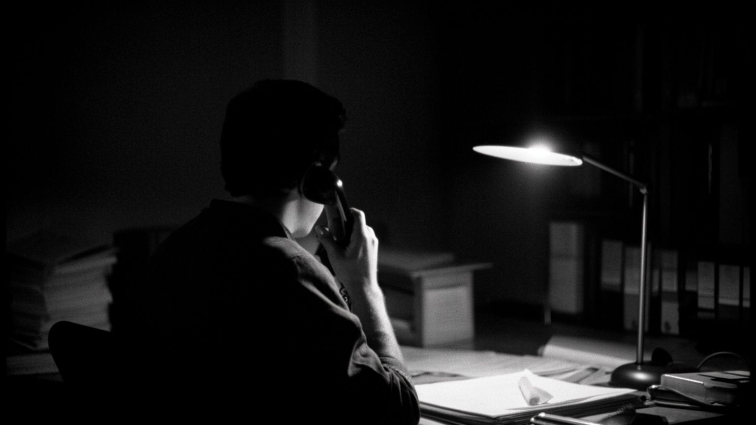 Pessoa de costas ao telefone, sob a luz de um abajur